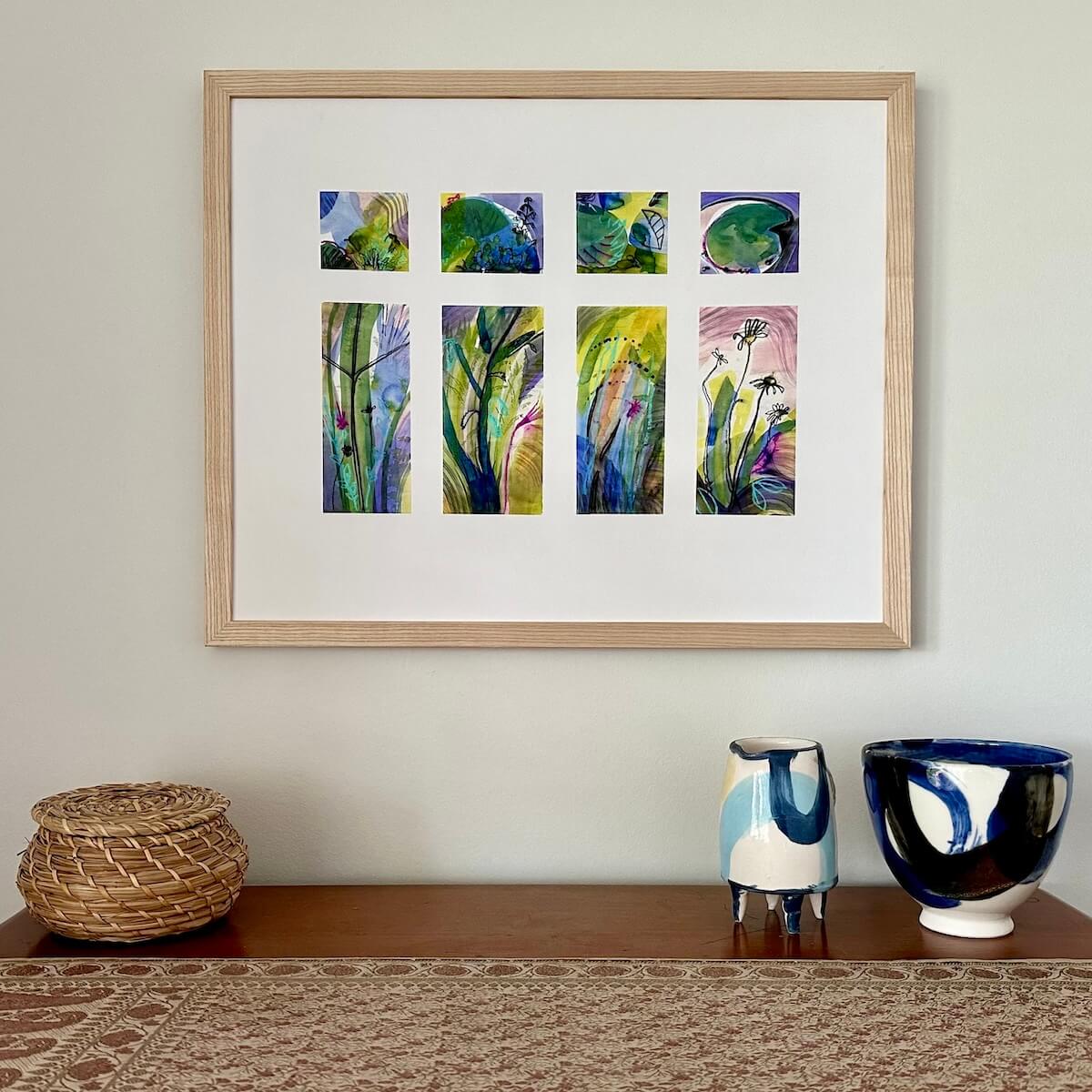 Drench, abstract botanical art print by artist Teresa Flavin, flower forms, leaves, lily pad and stems in gold, green, violet, magenta, blue and black, shown in light wood frame on wall.