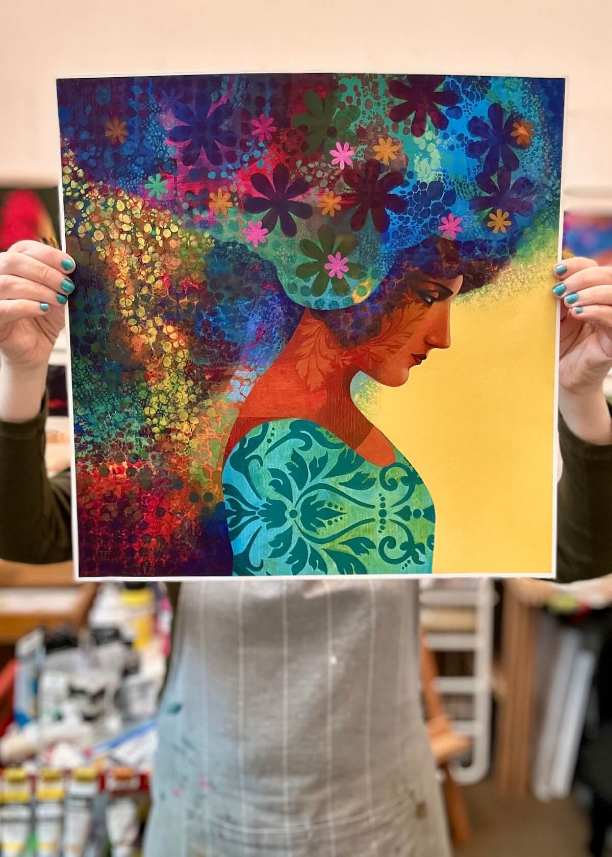 Person holding a colorful artwork of a woman with flowers in her hair.