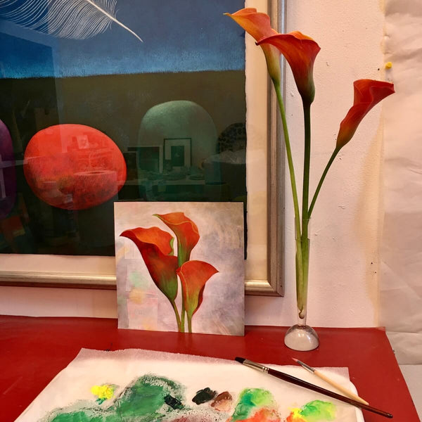 Teresa Flavin's Orange Calla Lilies painting on table in studio next to a paintbrush and palette with fresh calla lilies in vase.