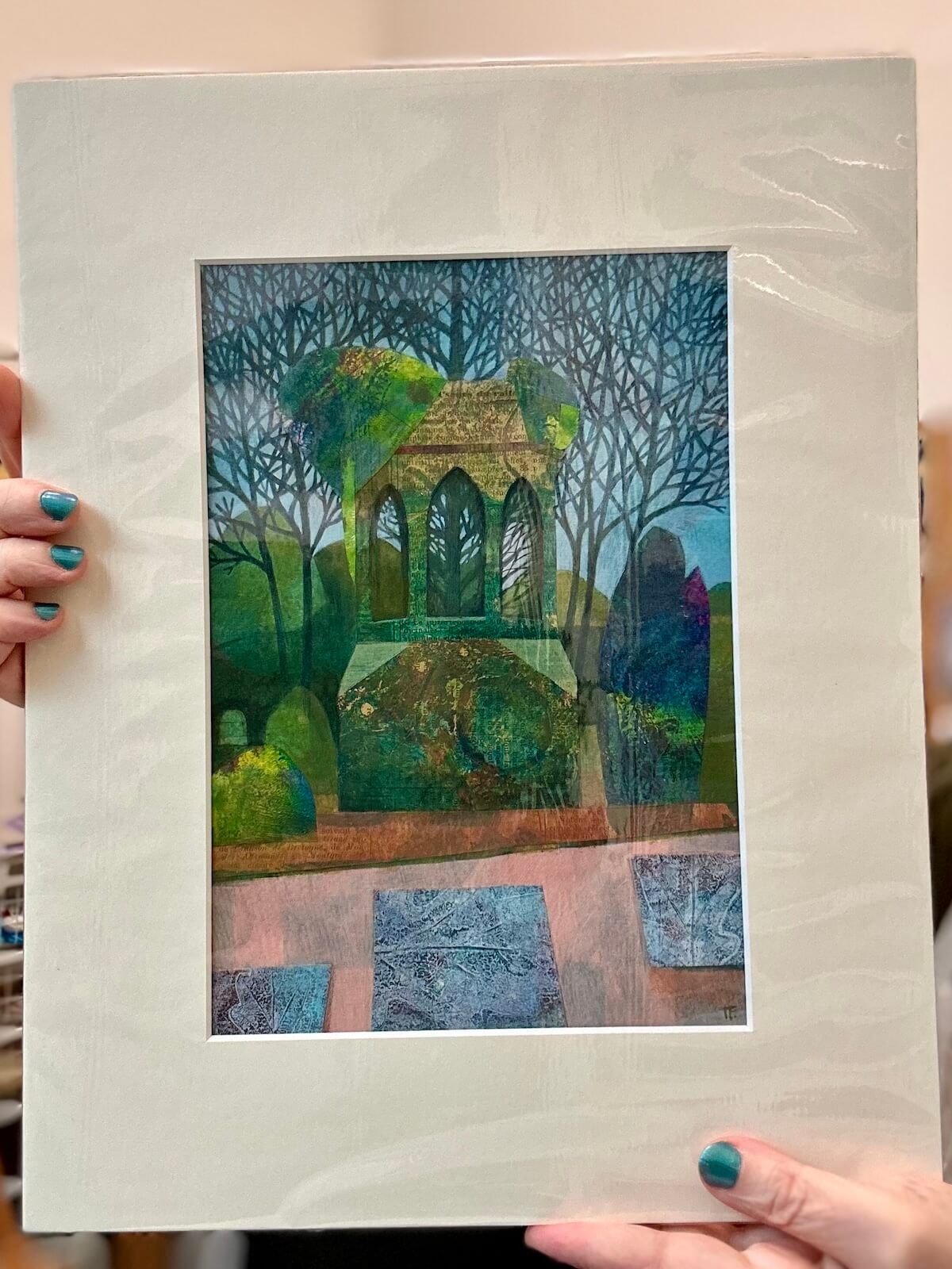 Mounted landscape artwork with a cupola and trees held by hands.