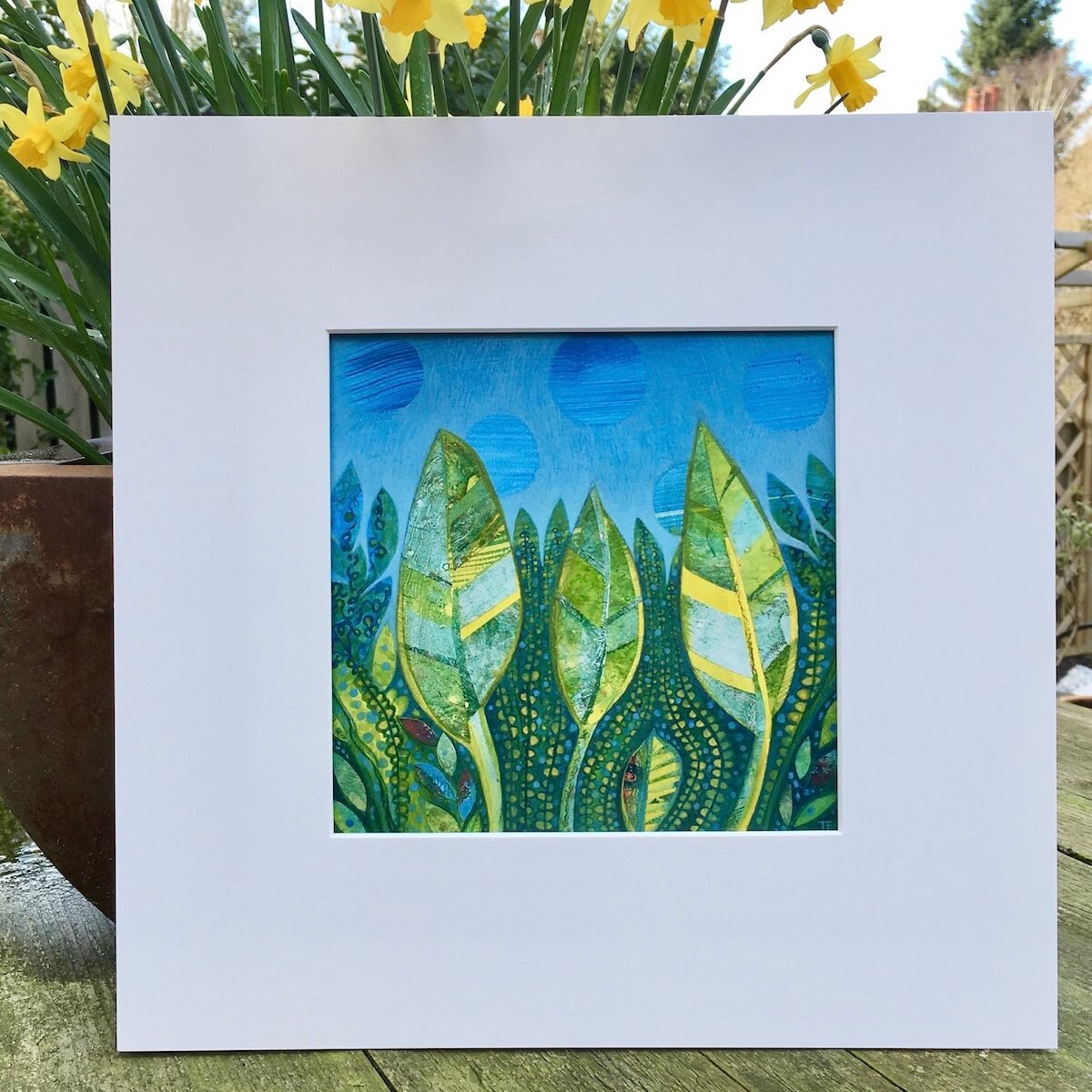 Rebirth painting by Teresa Flavin shown in white mountboard outside next to a plant pot.