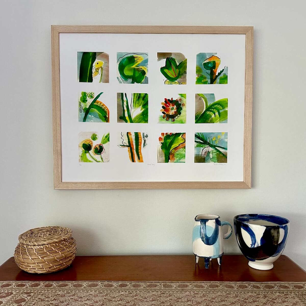 Good Day, abstract botanical art print by artist Teresa Flavin, flower forms, leaves, lily pad and stems in gold, green, orange and blue, in light wood frame on wall.