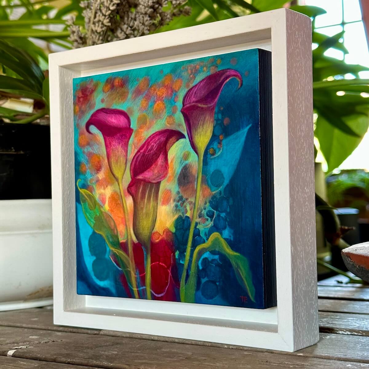 Side view of Magenta Callas painting by Teresa Flavin on a wood table with plants.