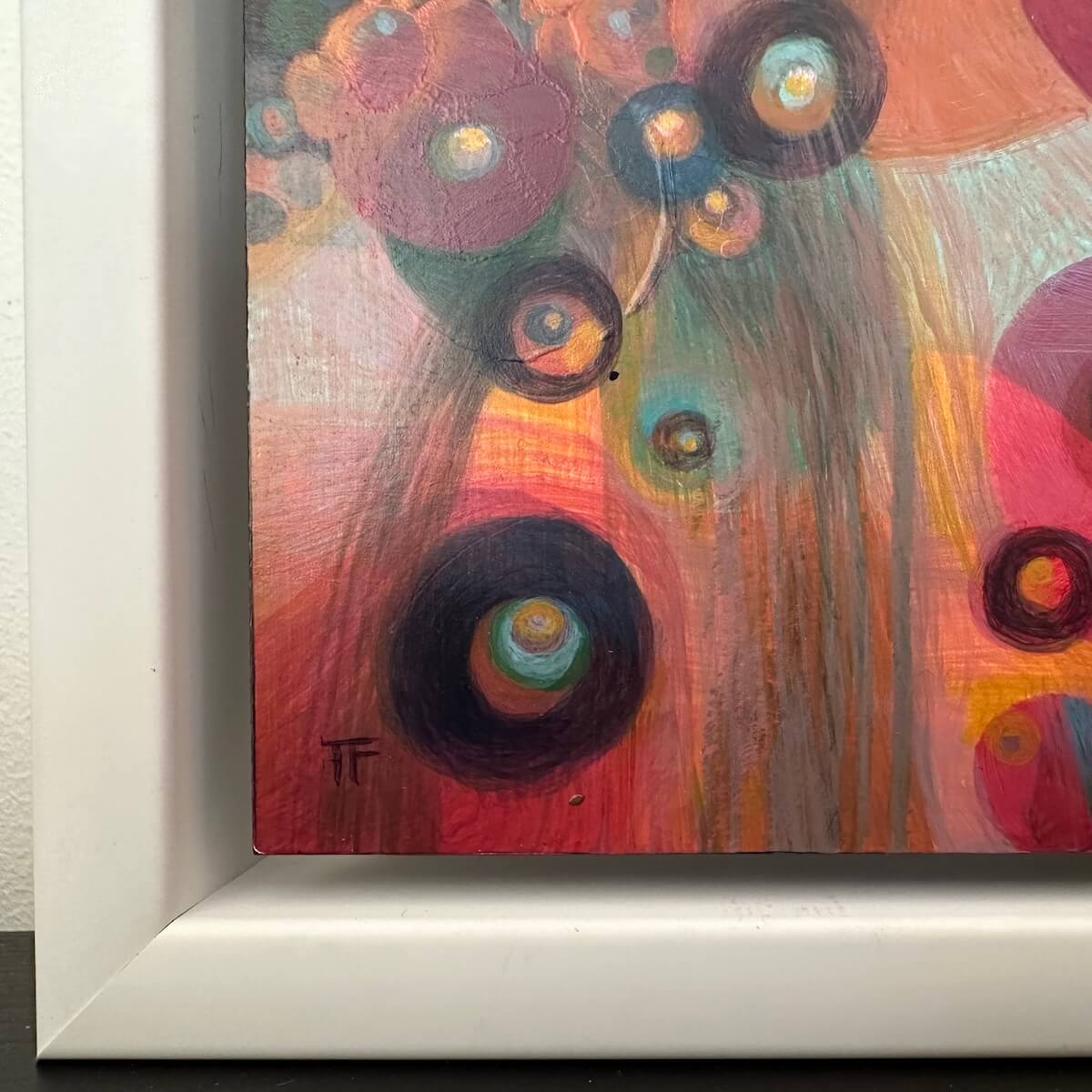 Close-up of art piece with vibrant colors and circular patterns framed on a white wall.