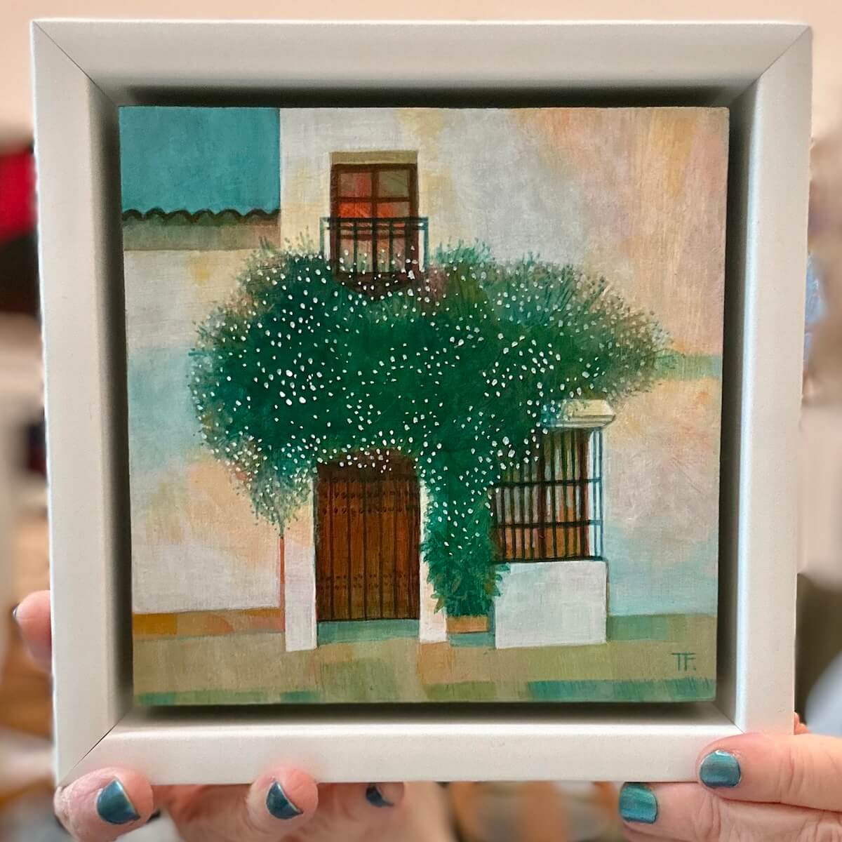 Framed artwork of a building with greenery held by a person.