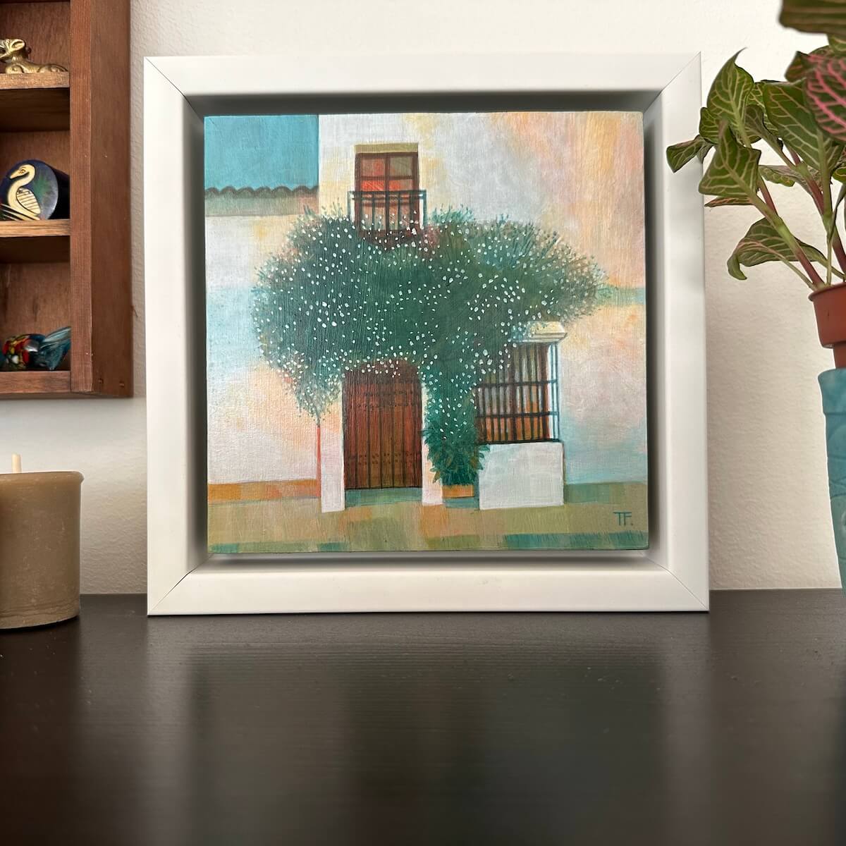 Framed painting of a street scene with trees and buildings on a table.
