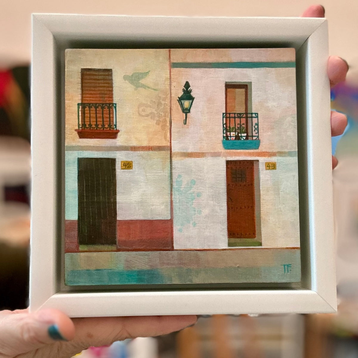 Framed artwork of a Spanish street scene with buildings and doors.
