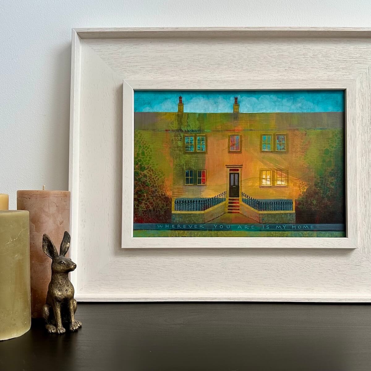 Framed artwork of Bronte Birthplace with candles and a rabbit figurine on a surface.