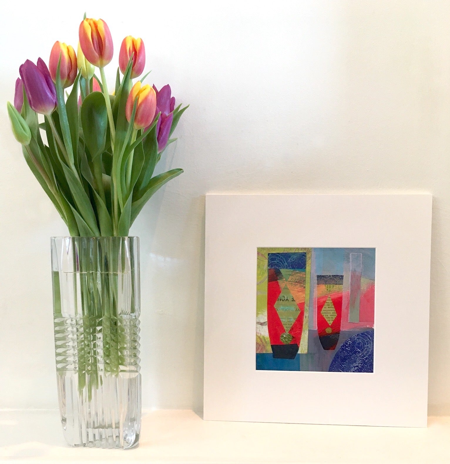 Two Diamonds by Teresa Flavin Artist, abstract still life mixed media painting shown in white mount on shelf next to tulips in vase.